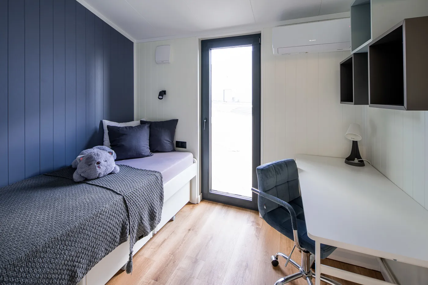 Interieur Modulodge model VELD eenpersoons slaapkamer met bed, bureau en deur naar buiten met daglicht